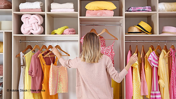 Person ordnet Kleidung in einem offenen Kleiderschrank.
