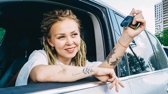 Frau schaut mit Autoschlüssel in der Hand aus Autofenster