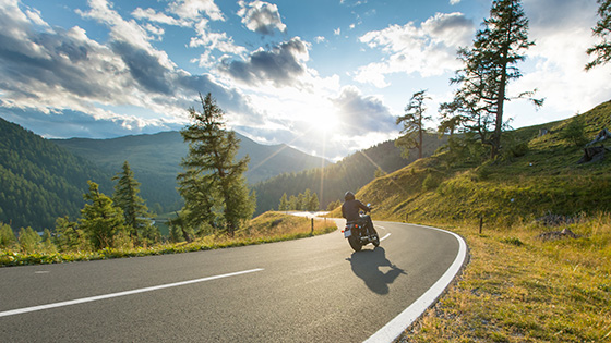 Motorradfahrer fährt auf einer Straße der Sonne entgegen. Bergkulisse