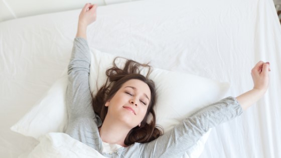 Aufwachen. Frau liegt im Bett und streckt sich.