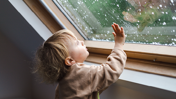 Kleinkind schaut wie Schnee auf das Dachfenster fällt