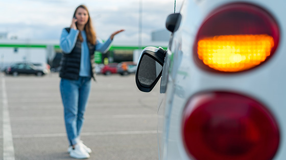Seitenspiegel hängt vom Auto. Im Hintergrund telefoniert eine Frau.