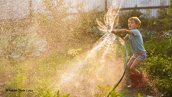 Person bewässert einen Garten mit einem Wasserschlauch.