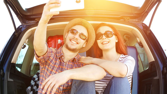 Mann und Frau sitzen im Kofferraum und machen ein Selfie