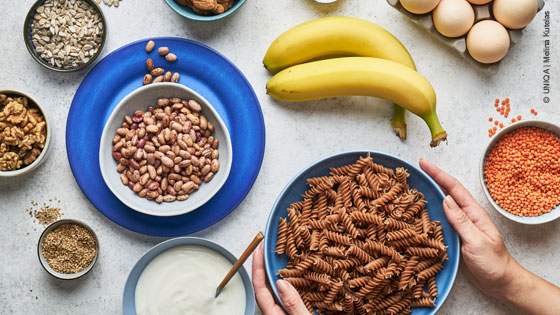 Diverse Nahrungsmittel in Schüsseln darunter Bananen, Nudeln, Bohnen, Eier und Linsen