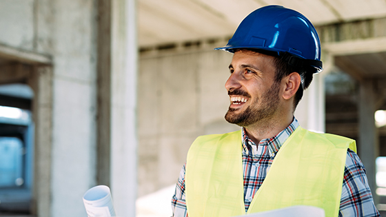 Mann mit Bauhelm und Plänen in der Hand auf der Baustelle