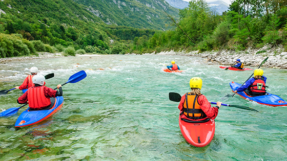 Eine Gruppe an Menschen fährt mit dem Kajak einen Fluss entlang.