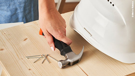 Hammer, Nägel und Schutzhelm auf einem Holzbrett