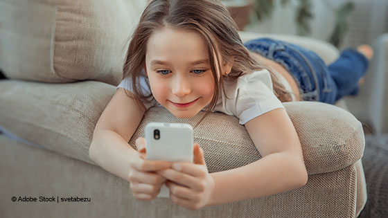 Kind liegt auf einem Sofa und schaut auf ein Smartphone.