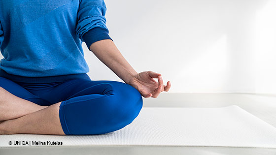 Person sitzt im Schneidersitz auf einer Yogamatte.