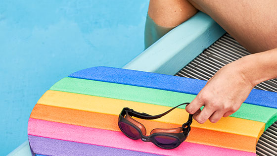 Schwimmbrille und buntes Schwimmbrett am Beckenrand
