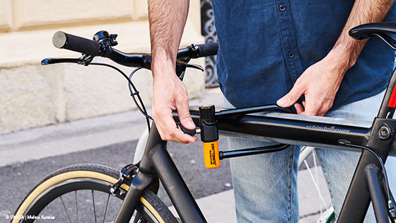 Person sichert ein schwarzes Fahrrad mit einem Bügelschloss am Rahmen.