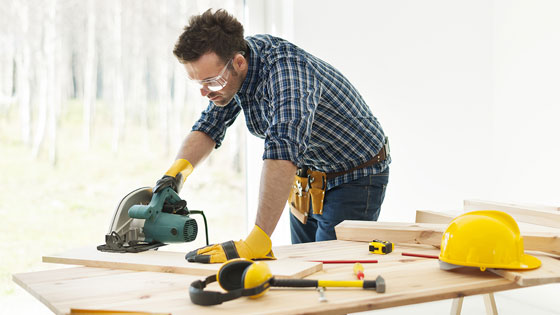 Person arbeitet mit einer Handkreissäge an einer Holzplatte auf einer Werkbank.