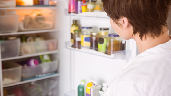Sicht auf eine geöffnete Kühlschranktür mit Lebensmitteln und Getränken, davor steht eine Person und blickt in den Kühlschrank.