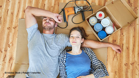 Ein paar liegt am Boden in der neuen Wohnung - neben Bohrmaschine und Dosen mit Farbe