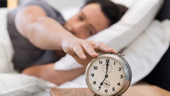 Mann im Bett wacht auf und schaltet den Wecker ab