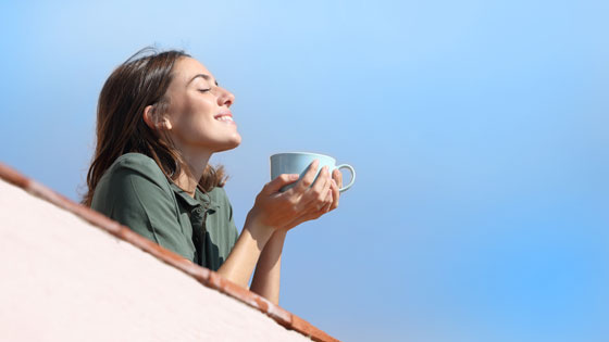 Frau hält Tasse Tee in der Hand und schaut genussvoll in die Sonne