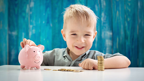 Kind lernt den Umgang mit Geld und spart für die Zukunft mit Sparschwein und Münzen.