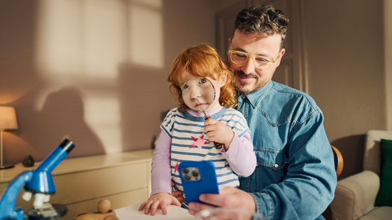 Papa und Kind begutachten das Smartphone mit der Lupe