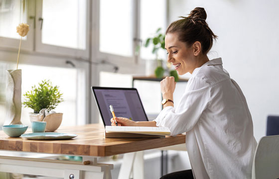 Junge Frau sitzt am Laptop und macht Notizen