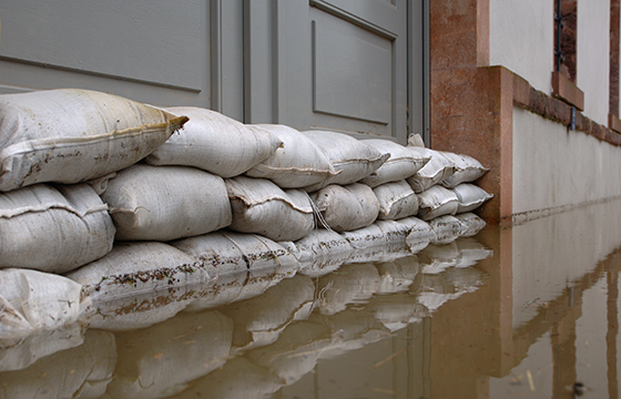 Mit Sandsäcken gesicherter Hauseingang während einer Überschwemmung mit stehendem Wasser vor dem Gebäude.