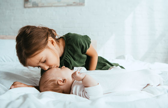 Kleinkind küsst Baby auf die Stirn.