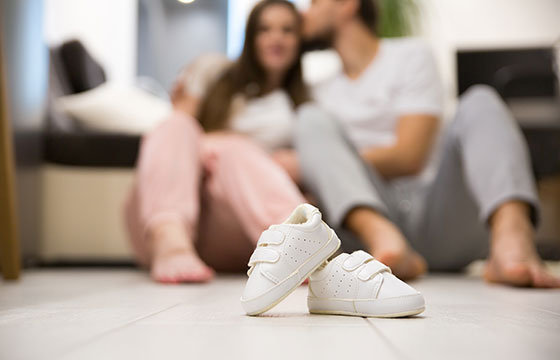 Babyschuhe stehen am Boden. Im Hintergrund sieht man ein Paar