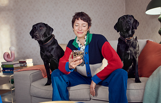 Frau sitzt mit ihren Hunden auf der Couch und liest am Handy