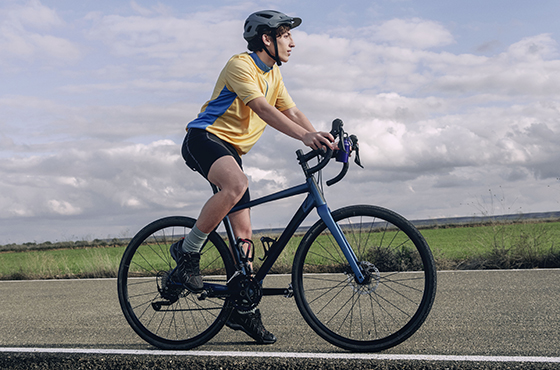 Dynamische Aufnahme einer Person auf einem Rennrad mit gelb-blauem Trikot und Helm – unterwegs durch eine grüne Landschaft unter dramatischem, wolkenverhangenem Himmel