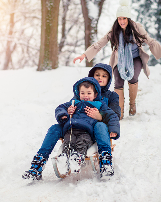 Mama mit Kindern im Schnee beim Rodeln