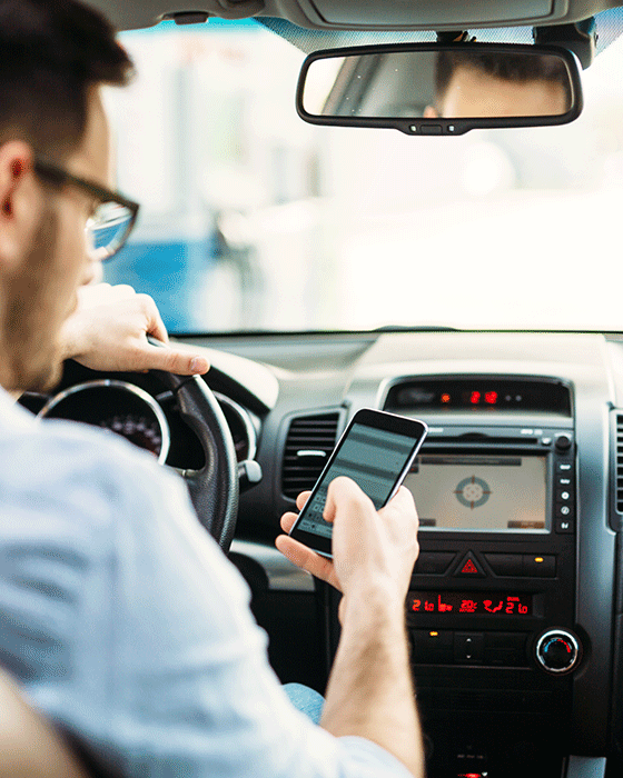 Mann im Auto schaut während der Fahrt auf sein Smartphone dass er in den Händen hält