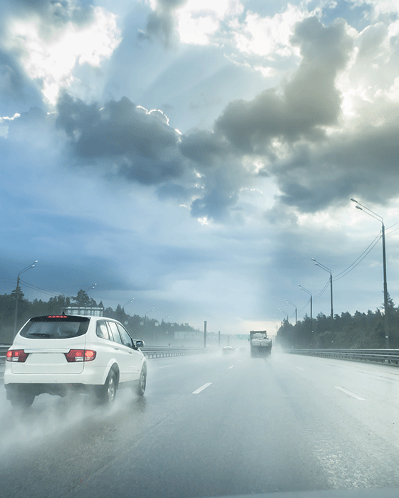 Schlechte Sicht und nasse Fahrbahn auf einer Straße. Im Hintergrund sind dicke dunkle Wolken zu sehen.