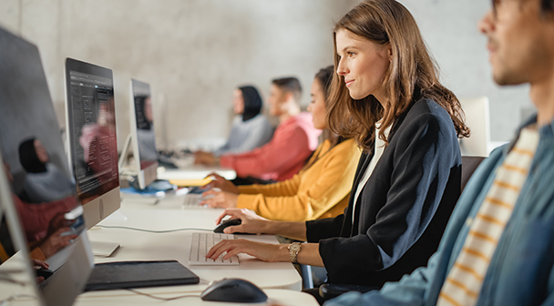 Mehrere Personen sitzen an einem langen Tisch vor ihren Computern