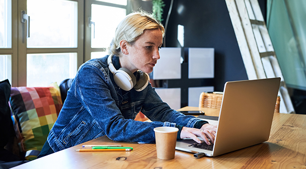 Frau sitzt mit Headset und Kaffee vor dem Laptop und tippt.