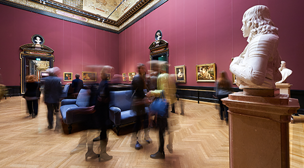 Besucher:innen betrachten Kunstwerke im Museum. Ölgemälde und Büsten sind abgebildet.