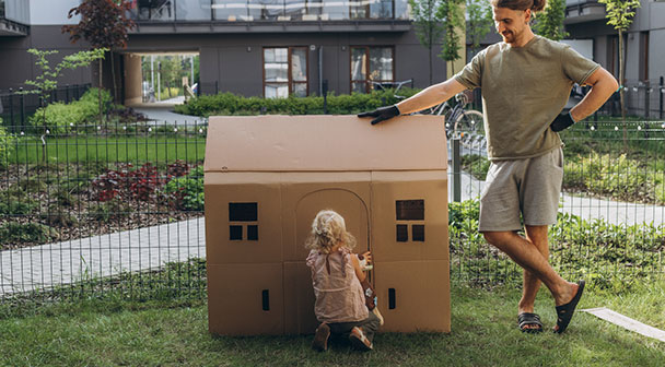 Vater und Kind haben im Garten ein kleines Haus aus Karton aufgestellt