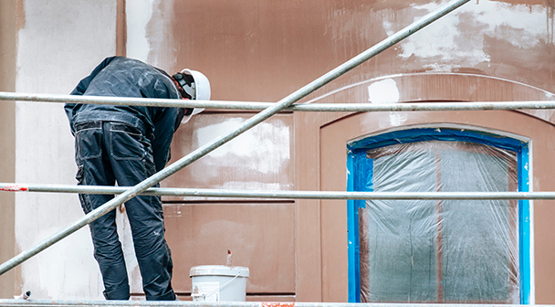 Maler auf dem Baugerüst verputzt die Wand eines Hauses