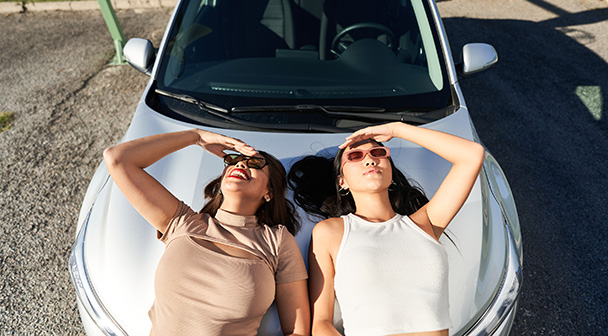 zwei Frauen lehnen an der Motorhaube und schauen in den Himmel