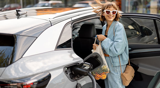 Frau tankt E-Auto auf und hebt die Einkaufstasche in das Auto