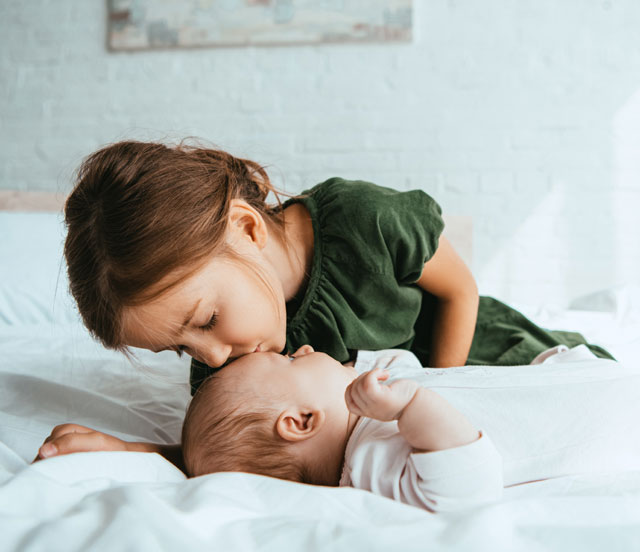 Kleinkind küsst Baby auf die Stirn.