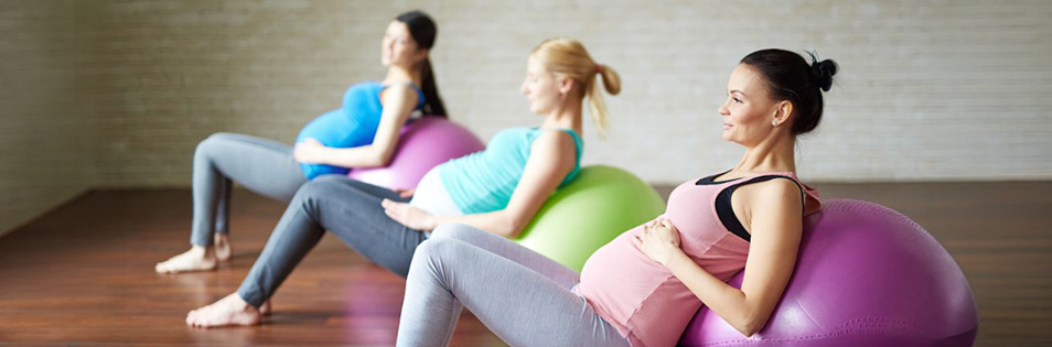 Drei schwangere Personen sitzen auf Gymnastikbällen in einem Bewegungsraum.