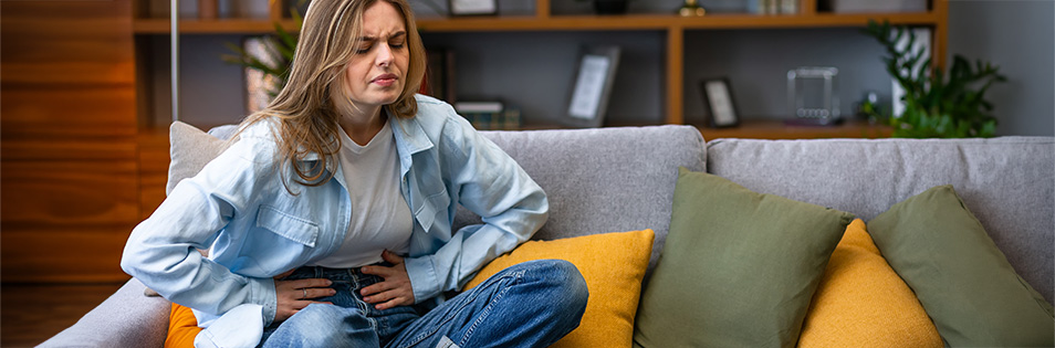 Frau sitzt auf der Couch und hält den Bauch fest