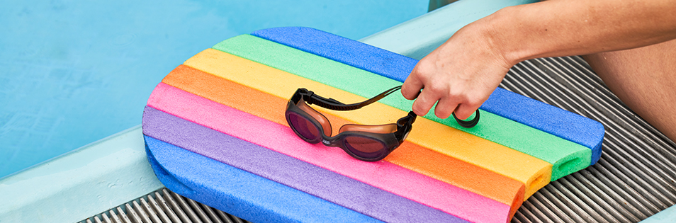 Schwimmbrille und buntes Schwimmbrett am Beckenrand