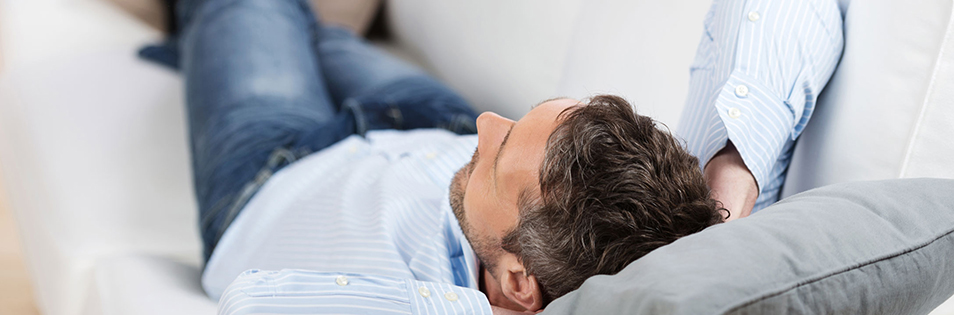 Person liegt auf einem Sofa und ruht mit dem Kopf auf einem Kissen.