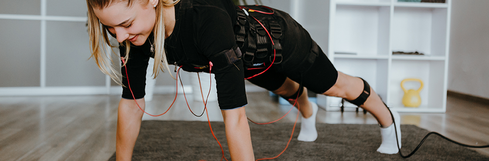 Training mit EMS-Anzug während einer Plank-Übung in einem Fitness- und Therapieraum.