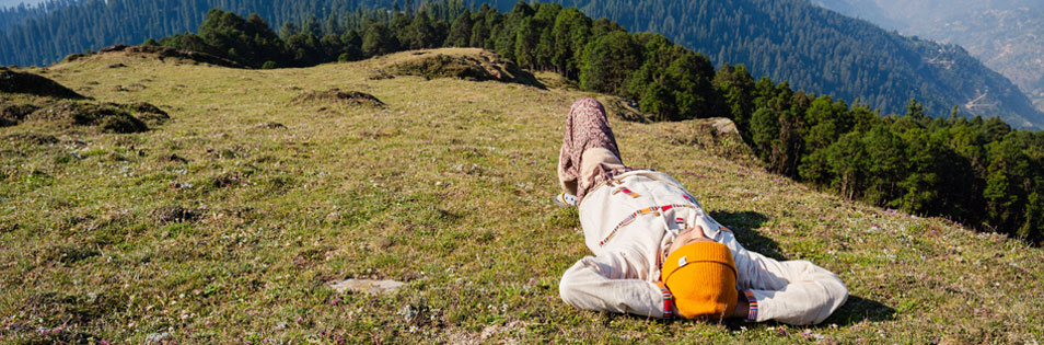 Person liegt in einer Wiese. Im Hintergrund sind Berge.