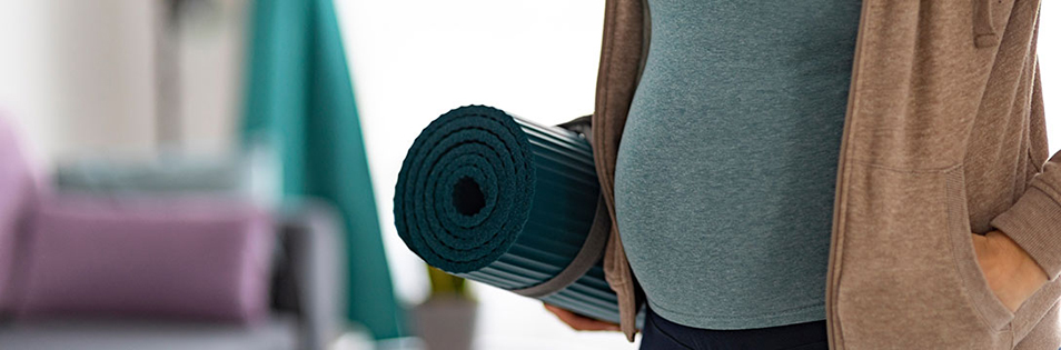 Schwangere Person hält eine zusammengerollte Gymnastikmatte unter dem Arm.