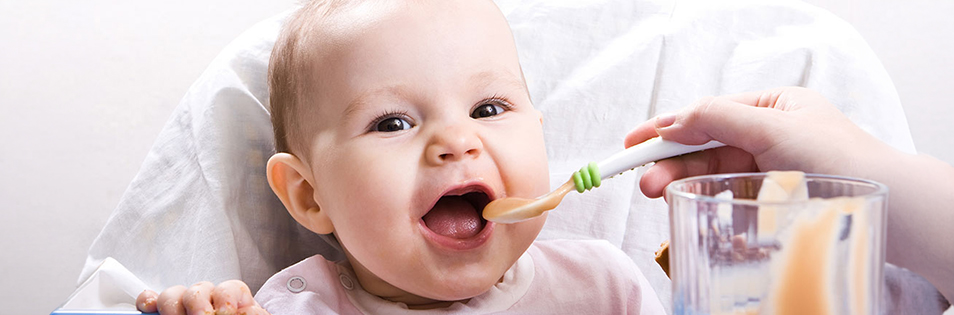 Baby sitzt in einem Hochstuhl und wird mit einem Löffel gefüttert.