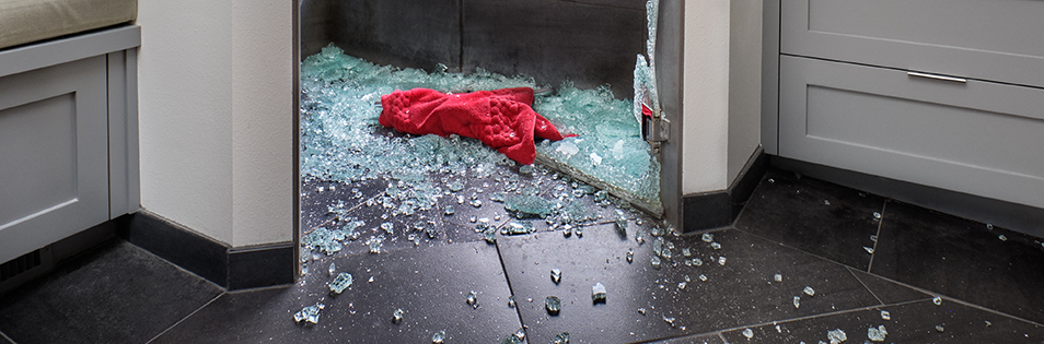 Zerbrochene Glasscheibe mit Glassplittern auf dem Boden einer Wohnung.