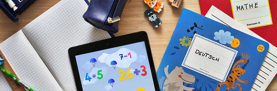 Tablet mit Lernanwendung liegt zwischen Schulheften, einem Deutschheft und weiteren Schulsachen auf einem Tisch.